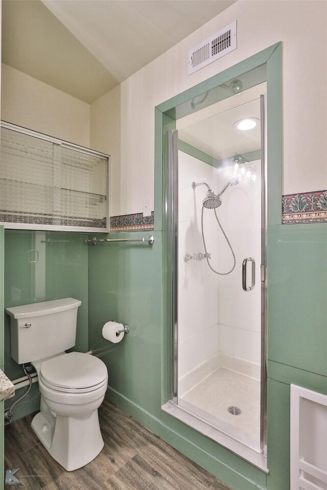 bathroom with hardwood / wood-style floors, a shower with door, and toilet