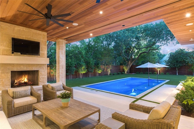 view of pool with an outdoor stone fireplace, ceiling fan, a patio area, and a yard