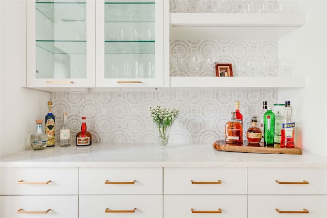 bar with decorative backsplash, light stone counters, and white cabinetry