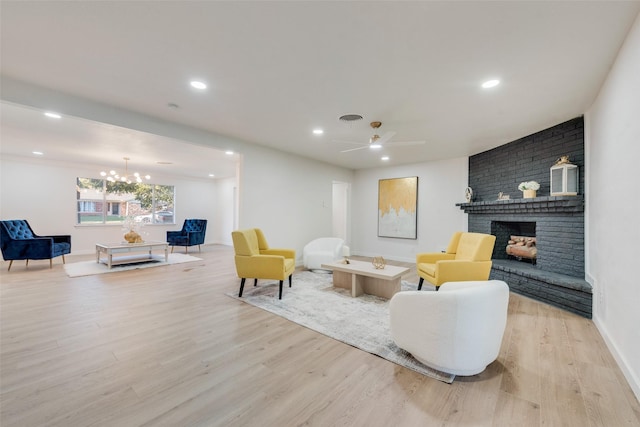 living room featuring a fireplace, light hardwood / wood-style flooring, and ceiling fan with notable chandelier