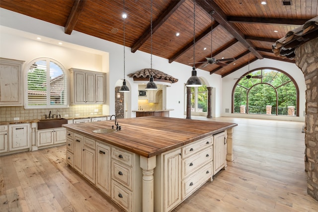 kitchen with a kitchen island with sink, cream cabinets, hanging light fixtures, light hardwood / wood-style flooring, and tasteful backsplash