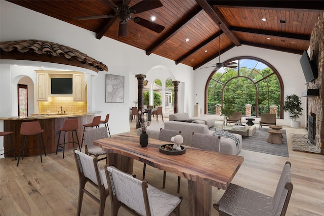 dining area with wooden ceiling, arched walkways, light wood finished floors, and high vaulted ceiling