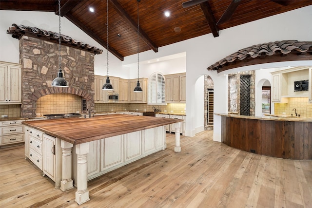 kitchen with light wood finished floors, butcher block countertops, arched walkways, and stainless steel microwave