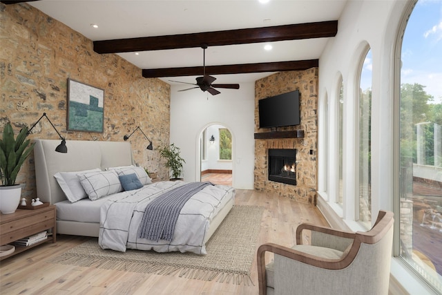 bedroom featuring arched walkways, ensuite bathroom, a fireplace, wood finished floors, and beamed ceiling