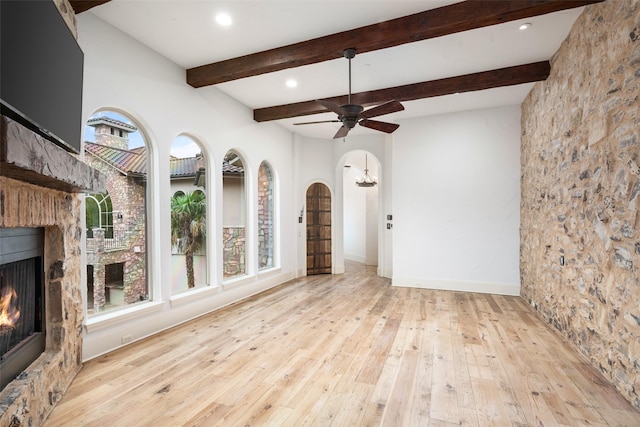 unfurnished living room featuring a lit fireplace, arched walkways, ceiling fan, and hardwood / wood-style floors