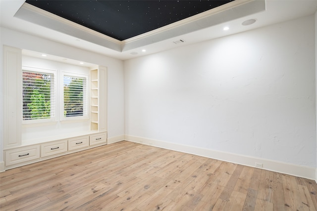 unfurnished room featuring built in shelves, a tray ceiling, and light hardwood / wood-style flooring