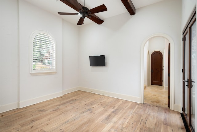 empty room featuring arched walkways, light wood finished floors, beam ceiling, and baseboards