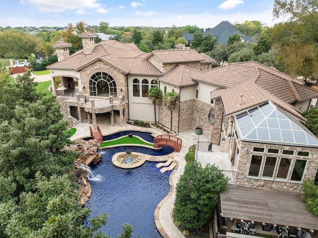 back of house with a balcony, stone siding, a tile roof, a patio area, and stucco siding