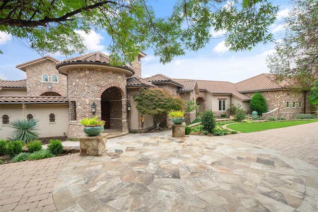 mediterranean / spanish house with stone siding, a patio, a chimney, and stucco siding