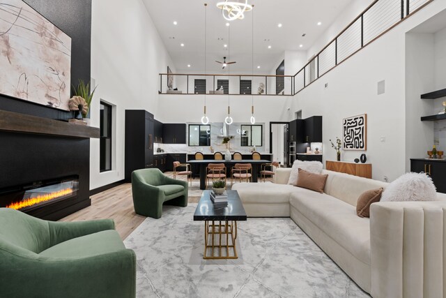 living room featuring built in shelves, ceiling fan, a high ceiling, and light hardwood / wood-style flooring