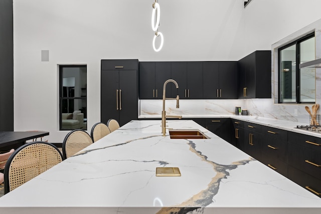 kitchen with a large island with sink, pendant lighting, light stone counters, and a breakfast bar area