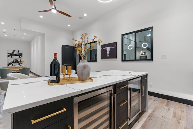 bar featuring light stone countertops, light wood-type flooring, beverage cooler, and ceiling fan