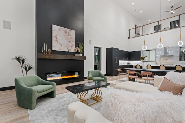 living room with a fireplace, a towering ceiling, light wood-type flooring, and ceiling fan