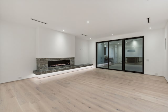 unfurnished living room featuring a stone fireplace and light hardwood / wood-style floors