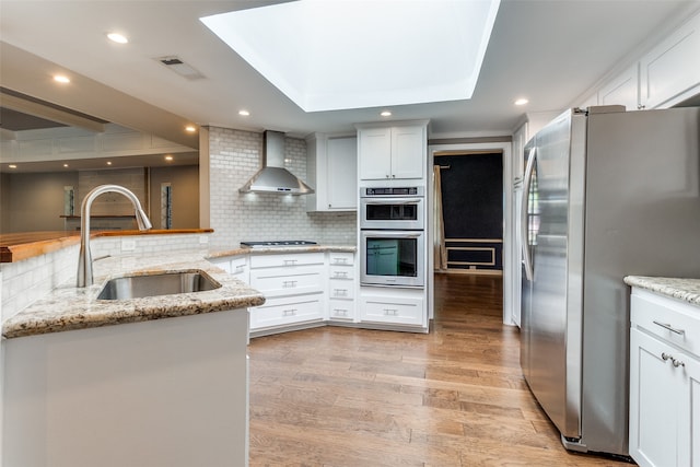 kitchen featuring white cabinetry, wall chimney exhaust hood, light wood-type flooring, and appliances with stainless steel finishes