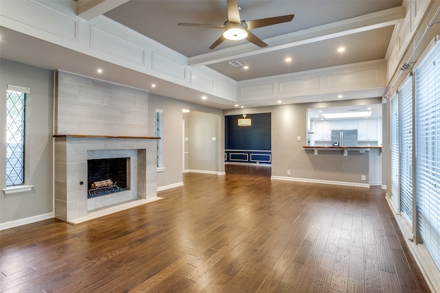 unfurnished living room with ceiling fan, dark wood-type flooring, and a tiled fireplace