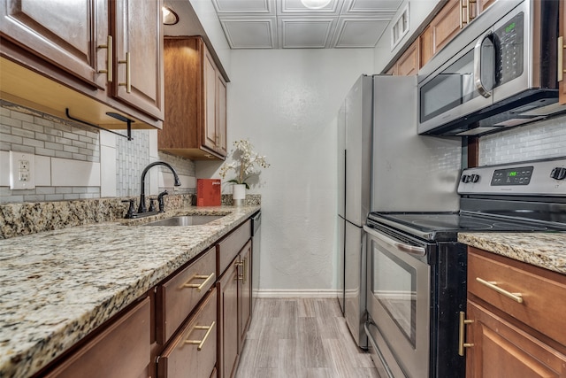 kitchen with decorative backsplash, light stone counters, stainless steel appliances, sink, and light hardwood / wood-style floors