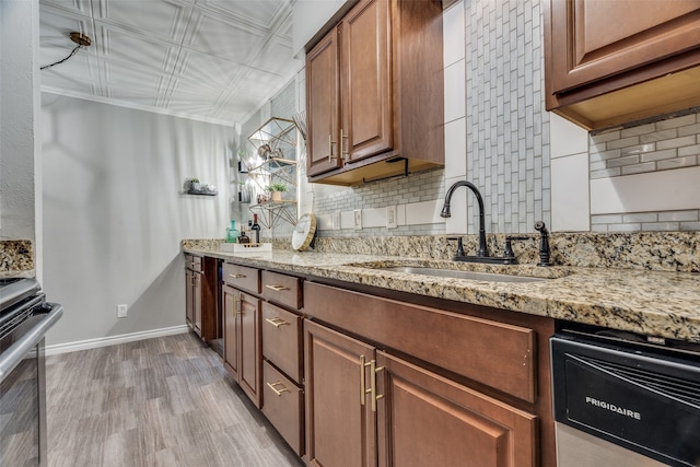 kitchen with decorative backsplash, light wood-type flooring, light stone counters, stainless steel appliances, and sink