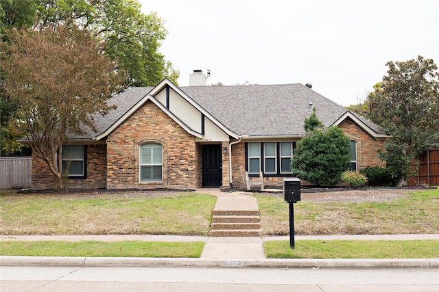 view of front of home with brick siding, a shingled roof, a chimney, fence, and a front yard