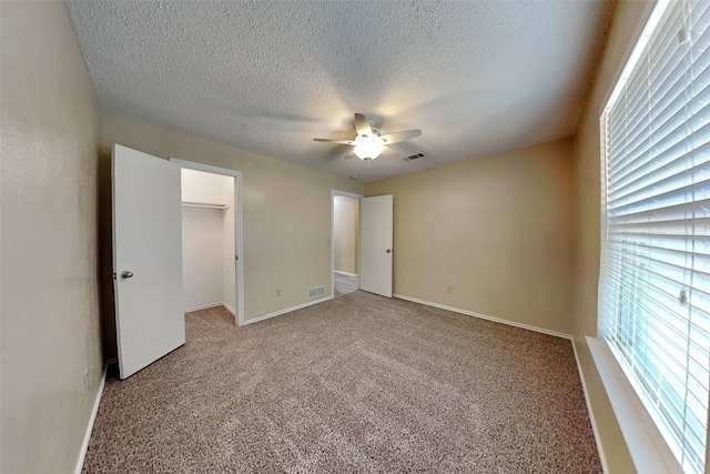 unfurnished bedroom featuring light carpet, a textured ceiling, a spacious closet, and ceiling fan