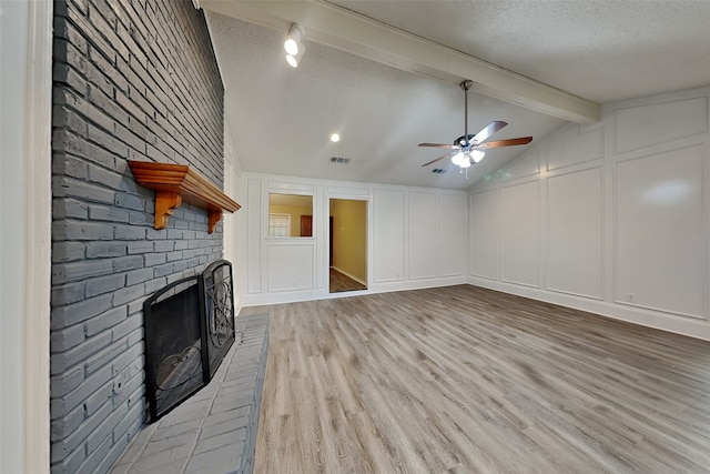 unfurnished living room with ceiling fan, a brick fireplace, lofted ceiling with beams, a textured ceiling, and light wood-type flooring