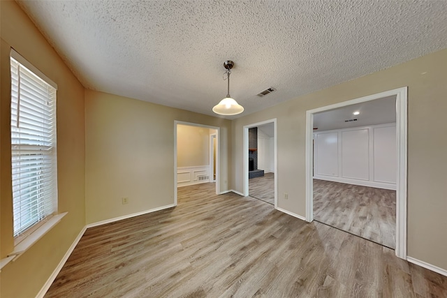 empty room featuring light hardwood / wood-style flooring, a textured ceiling, and a brick fireplace