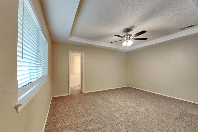 carpeted spare room featuring a tray ceiling, ceiling fan, and a textured ceiling