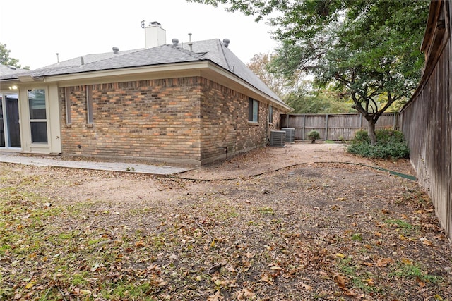 view of property exterior with a fenced backyard, a chimney, central AC, and brick siding