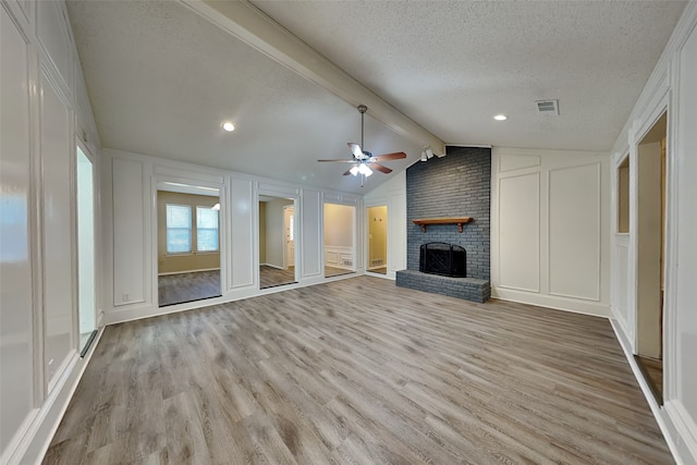 unfurnished living room featuring ceiling fan, vaulted ceiling with beams, light hardwood / wood-style flooring, a textured ceiling, and a fireplace