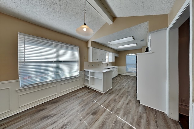 kitchen featuring lofted ceiling with beams, a textured ceiling, decorative light fixtures, light hardwood / wood-style floors, and white cabinetry