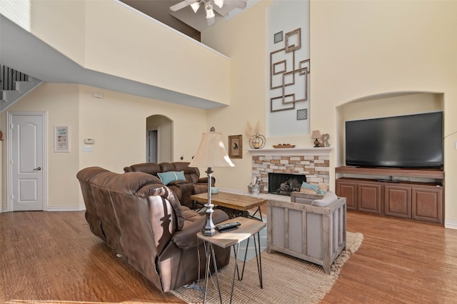 living room with light wood-type flooring, a towering ceiling, a fireplace, and ceiling fan