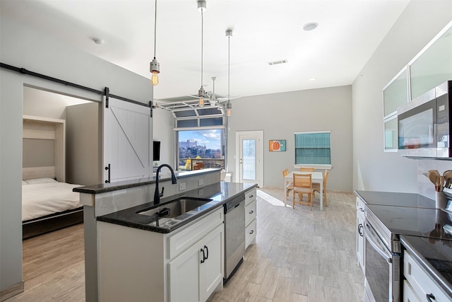 kitchen featuring white cabinets, sink, a barn door, appliances with stainless steel finishes, and decorative light fixtures