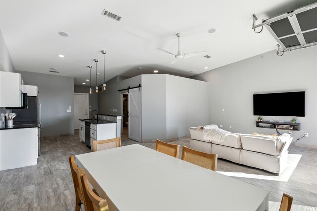 interior space with white cabinets, a barn door, hanging light fixtures, and an island with sink