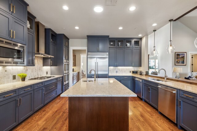 kitchen with sink, built in appliances, wall chimney exhaust hood, dark hardwood / wood-style floors, and decorative light fixtures