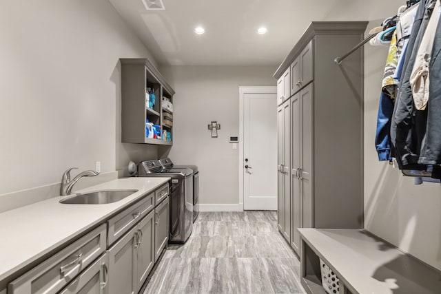 washroom with washing machine and clothes dryer, sink, cabinets, and light wood-type flooring