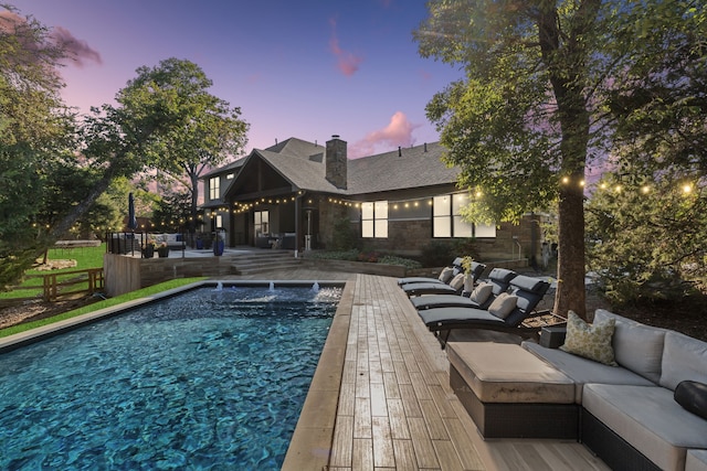 pool at dusk featuring outdoor lounge area, pool water feature, and a patio area