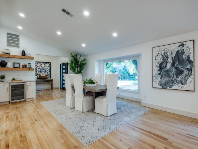 dining space with light hardwood / wood-style flooring, beverage cooler, and vaulted ceiling