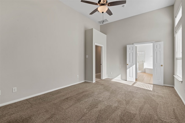 unfurnished bedroom with ceiling fan, light colored carpet, a towering ceiling, and connected bathroom