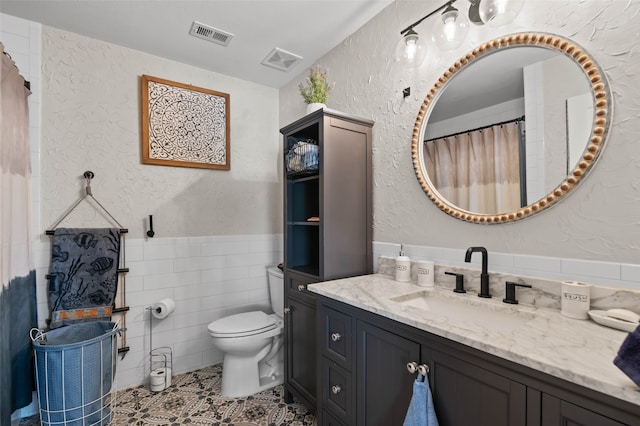 bathroom featuring tile patterned floors, vanity, toilet, and tile walls