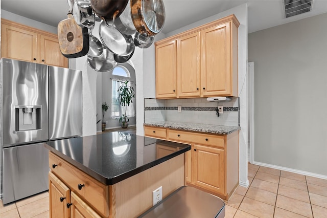 kitchen featuring light tile patterned floors, backsplash, stainless steel refrigerator with ice dispenser, dark stone counters, and light brown cabinets