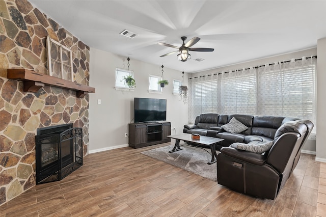 living room with a stone fireplace, wood-type flooring, and ceiling fan