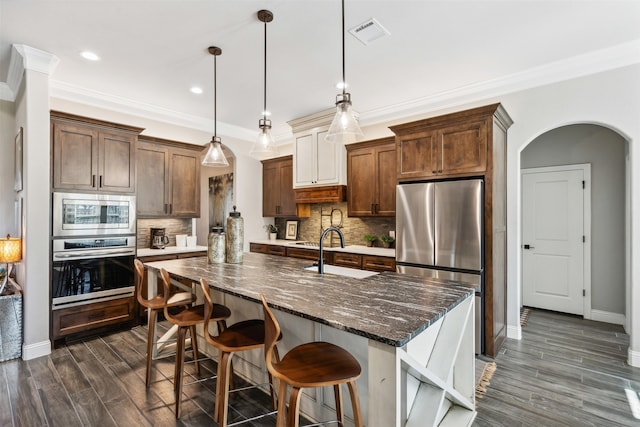 kitchen featuring decorative light fixtures, dark hardwood / wood-style flooring, stainless steel appliances, and an island with sink