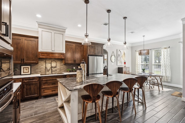 kitchen with pendant lighting, a kitchen island with sink, dark wood-type flooring, sink, and appliances with stainless steel finishes