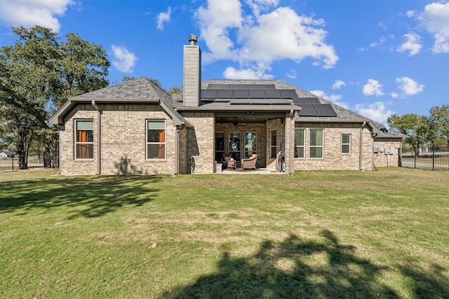 rear view of house with ceiling fan, a yard, a patio, and solar panels