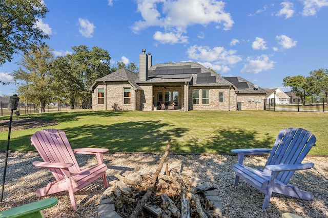 back of house featuring solar panels, a fire pit, a patio area, and a lawn