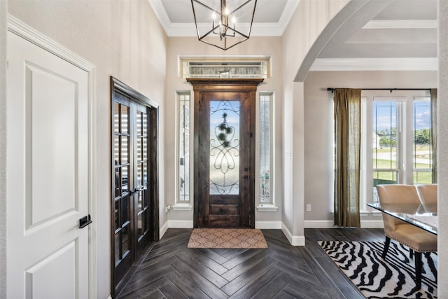 entrance foyer with a chandelier, dark parquet flooring, plenty of natural light, and ornamental molding