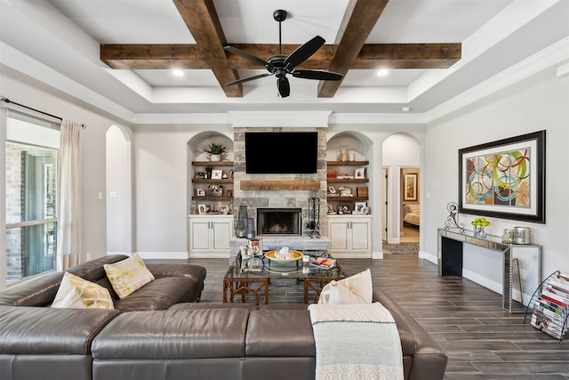 living room with ceiling fan, dark wood-type flooring, built in features, beamed ceiling, and a fireplace