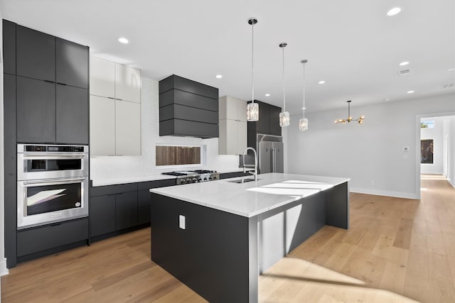 kitchen with a large island with sink, light wood-type flooring, decorative light fixtures, and premium range hood