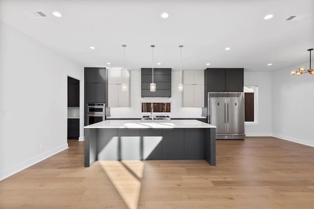 kitchen with appliances with stainless steel finishes, ventilation hood, a spacious island, decorative light fixtures, and light hardwood / wood-style floors