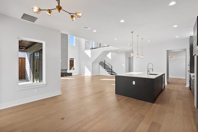 kitchen with sink, a notable chandelier, an island with sink, decorative light fixtures, and light wood-type flooring